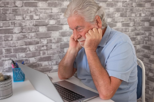 Serious worried businessman looking at laptop with hands on the face elderly male sitting at workplace