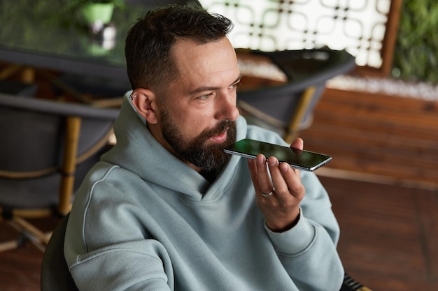 Serious young adult man in casual clothes in cafe records audio messages