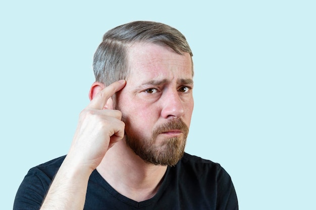 Serious young bearded man touches his forehead with his finger Focuses attention on the problem Isolated portrait on a pastel background