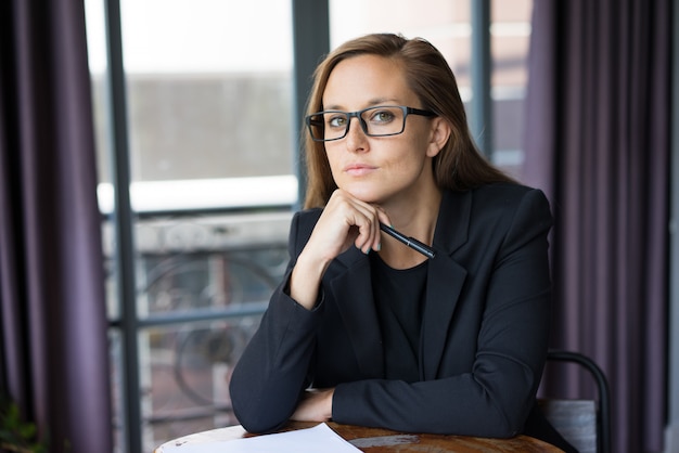 serious young beautiful brown-haired woman looking at camera, holding pen 