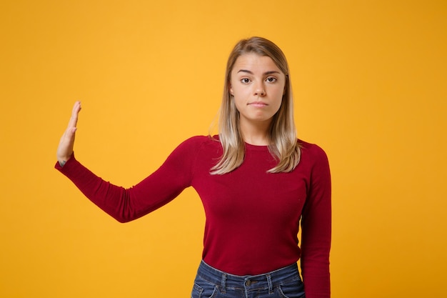 Serious young blonde woman in casual clothes posing isolated on yellow orange background studio portrait. People emotions lifestyle concept. Mock up copy space. Showing stop gesture with palm aside.