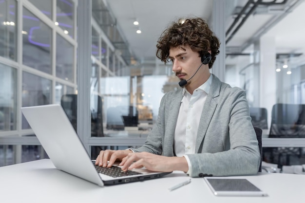 A serious young businessman man in a headset is sitting in the office at a desk and is concentrating