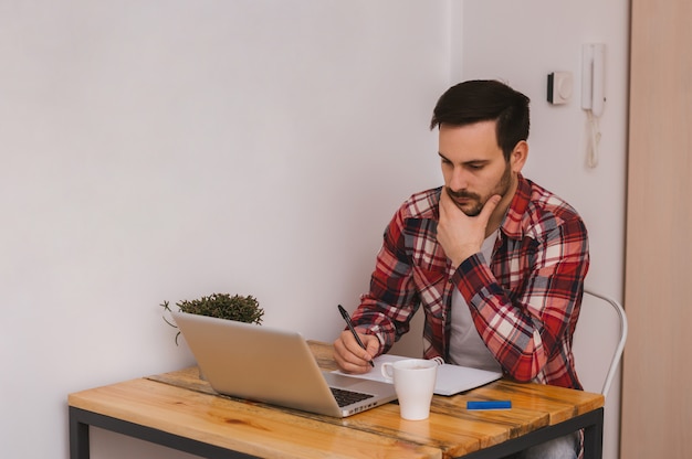 Serious young businessman  sitting and using laptop at office and taking notes