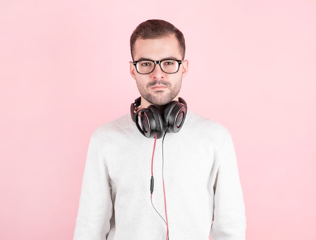 Serious young cute kid listening to music in big white headphones on pink wall, in white sweatshirt, world dj day