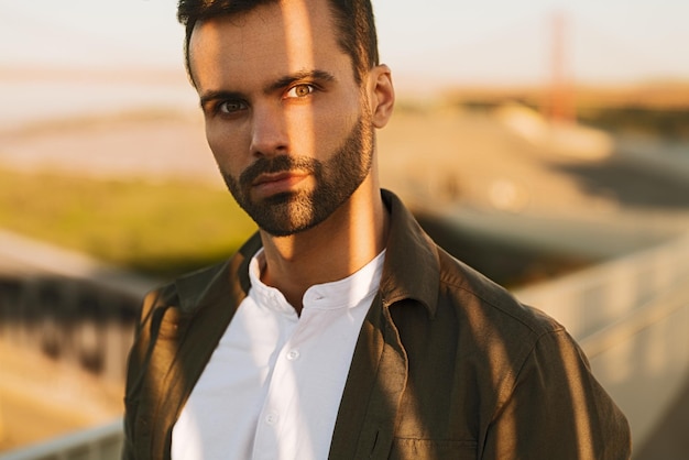 Serious young ethnic guy looking at camera on street at sunset