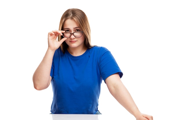 Serious young girl in a blue T-shirt adjusts his glasses. Education and knowledge. .