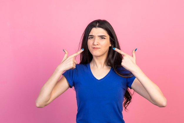 Serious young lady pointing her fingers to herself and standing on pink background High quality photo