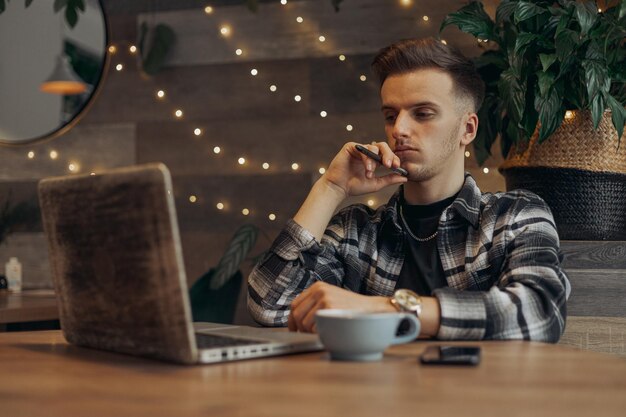 Serious young male freelancer using laptop and working on project while sitting at table in cafe