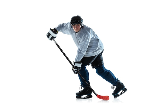 Serious young male hockey player with the stick on ice court and white wall