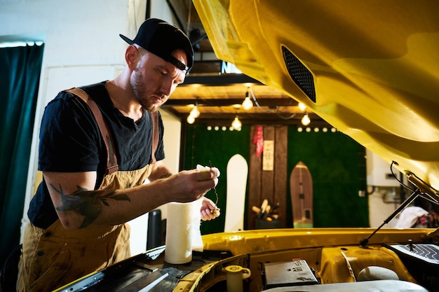 Serious young man in apron and cap wiping metallic wire with paper towel