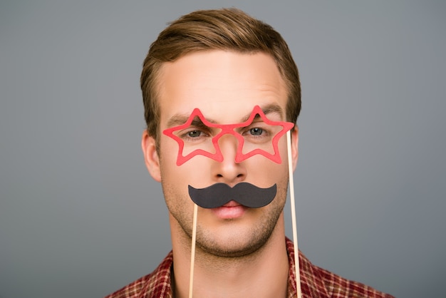 Serious young man posing with paper mustache and glasses like stars