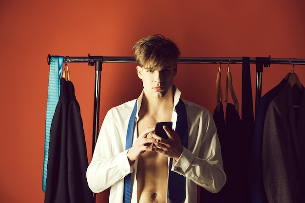 Serious young man with clothes on hanger with phone