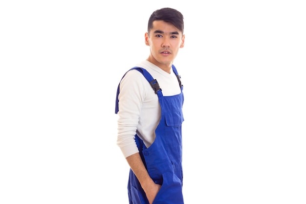 Serious young man with dark hair wearing in white shirt and blue overall on white background in studio