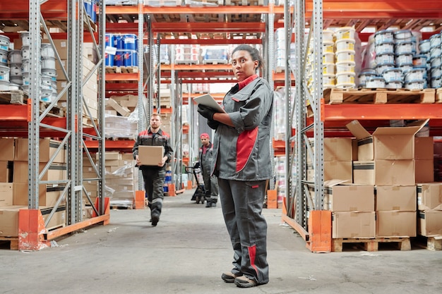 Serious young mixed-race woman in workwear and gloves entering data in tablet