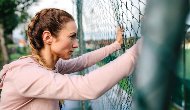 Serious young sportswoman with boxer braids leaning on a metal fence