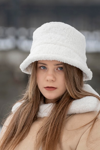 Serious young woman in fashionable white fur panama and beige sheepskin coat in winter outdoors Trendy youth outerwear