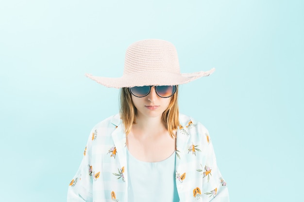 Serious young woman in summer clothes with pink straw hat and big round glasses