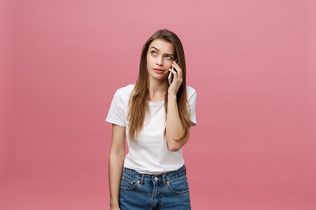 Serious young woman talking on phone isolated on pink. 