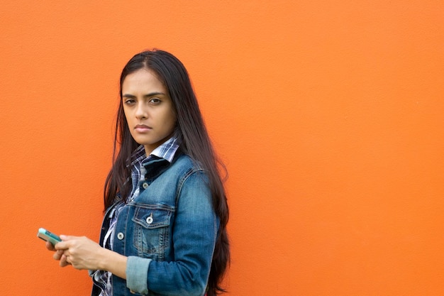 Serious Young Woman with cellphone While Standing Against Orange Wall Panama Central America