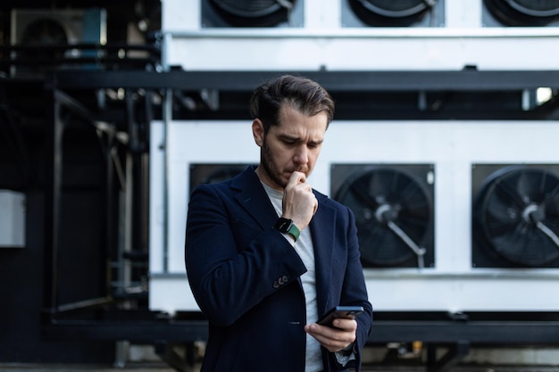 Seriously engineer stylish clothes with a mobile phone in his hands on the background of industrial