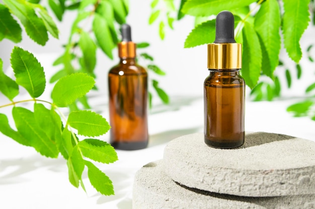 Serum essential oil tonic in a brown bottle on a white background with green leaves of the plant