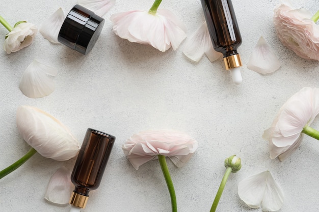 Serum and face cream on stone background with pink and white flowers