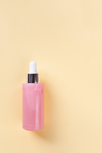 Serum for face or eye skin in beautiful pink bottle with dropper on yellow background