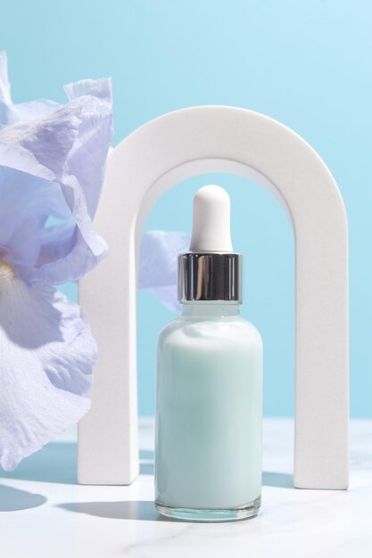 Serum with floral extracts for skincare in arch Nature cosmetics in glass bottle with pipette and iris flowers on blue background Face and body care spa concept