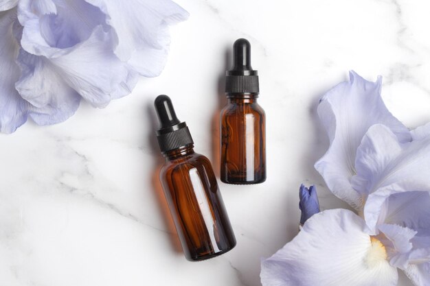 Serum with floral extracts for skincare Nature cosmetics in glass bottles with pipette and iris flowers on marble background Face and body care spa concept