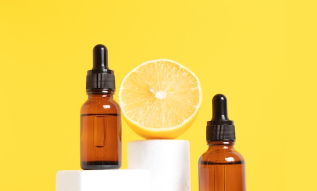 Serum with vitamin C Lemon essential oil Glass bottle with a pipette half a lemon on the podium yellow background Health and beauty concept Organic natural cosmetics