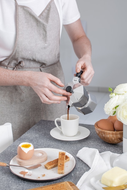 Served breakfast, toasted bread, soft boiled egg, female hands pouring coffee from moka