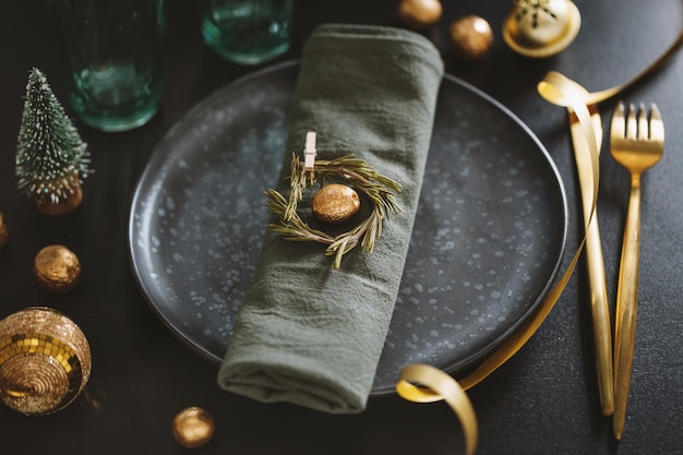 Served christmas table setting in dark tones with golden deco.