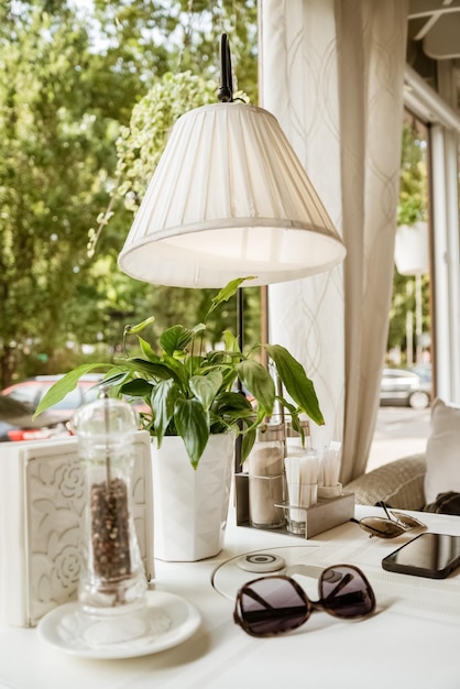 Served table decorated with lamp and green plant near window in cafe