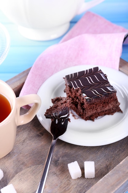 Served table with a cup of tea and chocolate cake on wooden background closeup