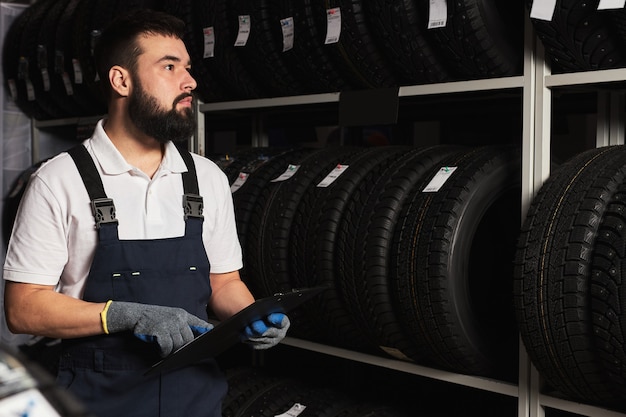 service staff bearded man examining tires in a supermarket mall, think about right trade for the size of the wheel, holding paper tablet in hands, checking