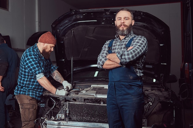 Service station. Two bearded brutal mechanics repairing a car in the garage.