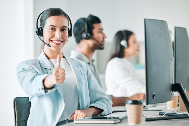 For service thats rated five stars. Portrait of a young call centre agent showing thumbs up while working in an office with her colleagues in the background.