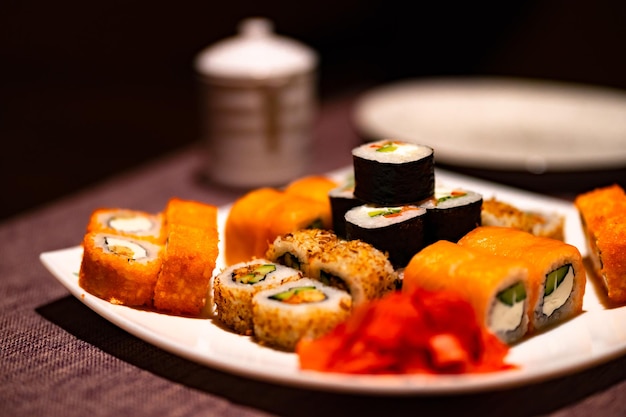 Serving of appetizing sushi on white plate in cafe Close up of set of tasty sushi rolls with wasabi and ginger in traditional Japanese restaurant