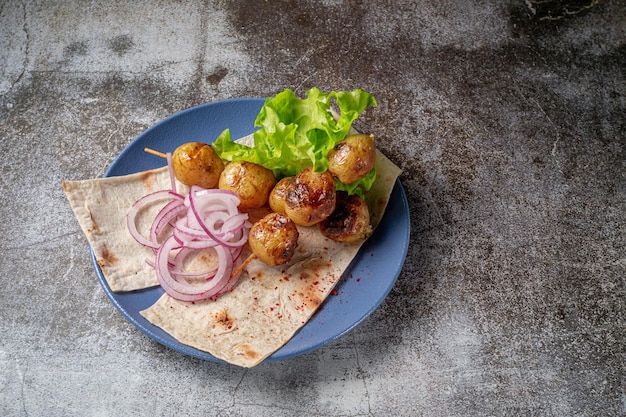 Serving a dish from a restaurant menu. Grilled country-style baked potatoes with pita bread, herbs and onions on a blue plate against the background of a gray stone table