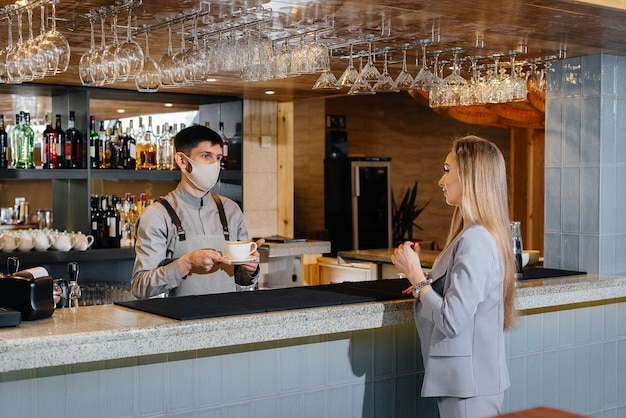 Serving a masked barista delicious natural coffee to a young girl in a beautiful cafe during a pandemic