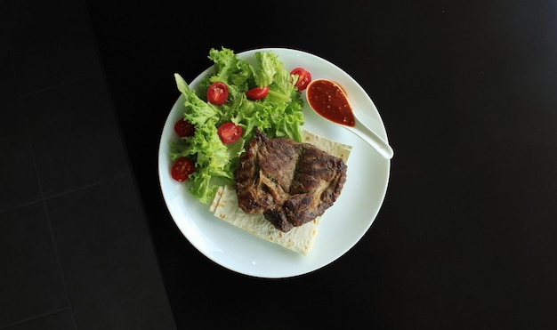 Serving of meat steak with sauce and fresh lettuce in a plate on black surface top view