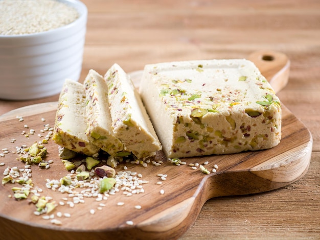 Sesame halva with pistachios on a teak chopping board on a brown wooden background