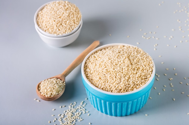 Sesame seeds in bowls and in a wooden spoon on a gray background Organic food