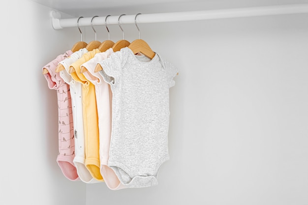 Set of baby bodysuits for a newborn girl and boy on hangers in white wardrobe. Motherhood, cleaning home kids wardrobe. Minimal fashion concept.