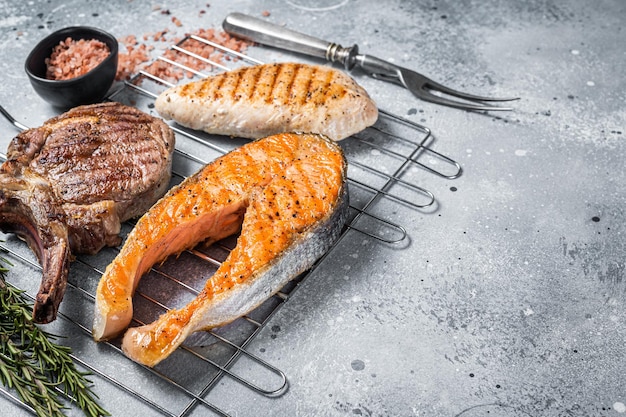 Set of bbq grilled meat steaks salmon, beef and turkey on a grill. Gray background. Top view. Copy space.