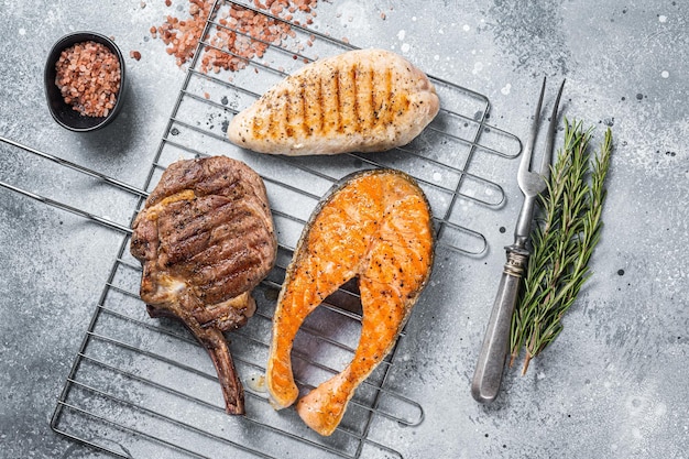 Set of bbq grilled meat steaks salmon, beef and turkey on a grill. Gray background. Top view.