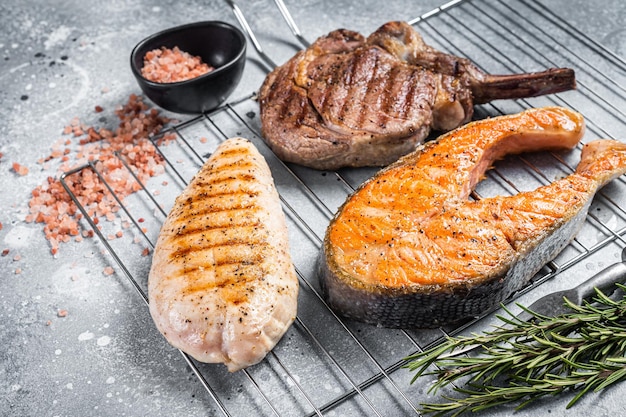 Set of bbq grilled meat steaks salmon beef and turkey on a grill Gray background Top view