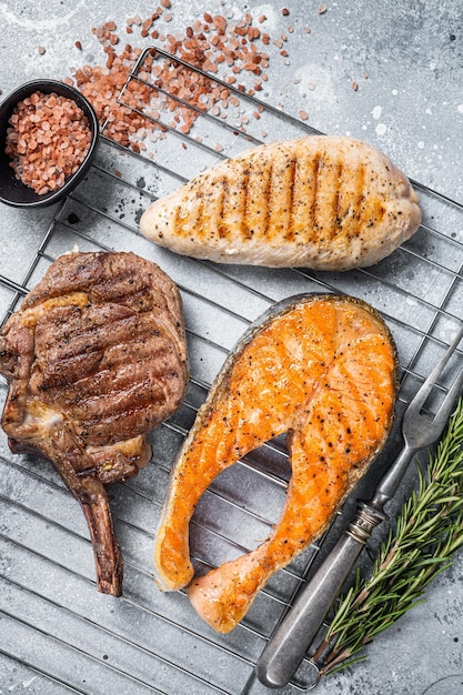 Set of bbq grilled meat steaks salmon beef and turkey on a grill Gray background Top view