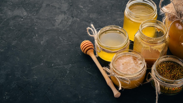 Photo a set of beekeeping products and honey on a black stone background free space for text top view