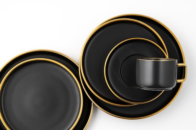 A set of black and golden ceramic plates and cup on a white background Top view